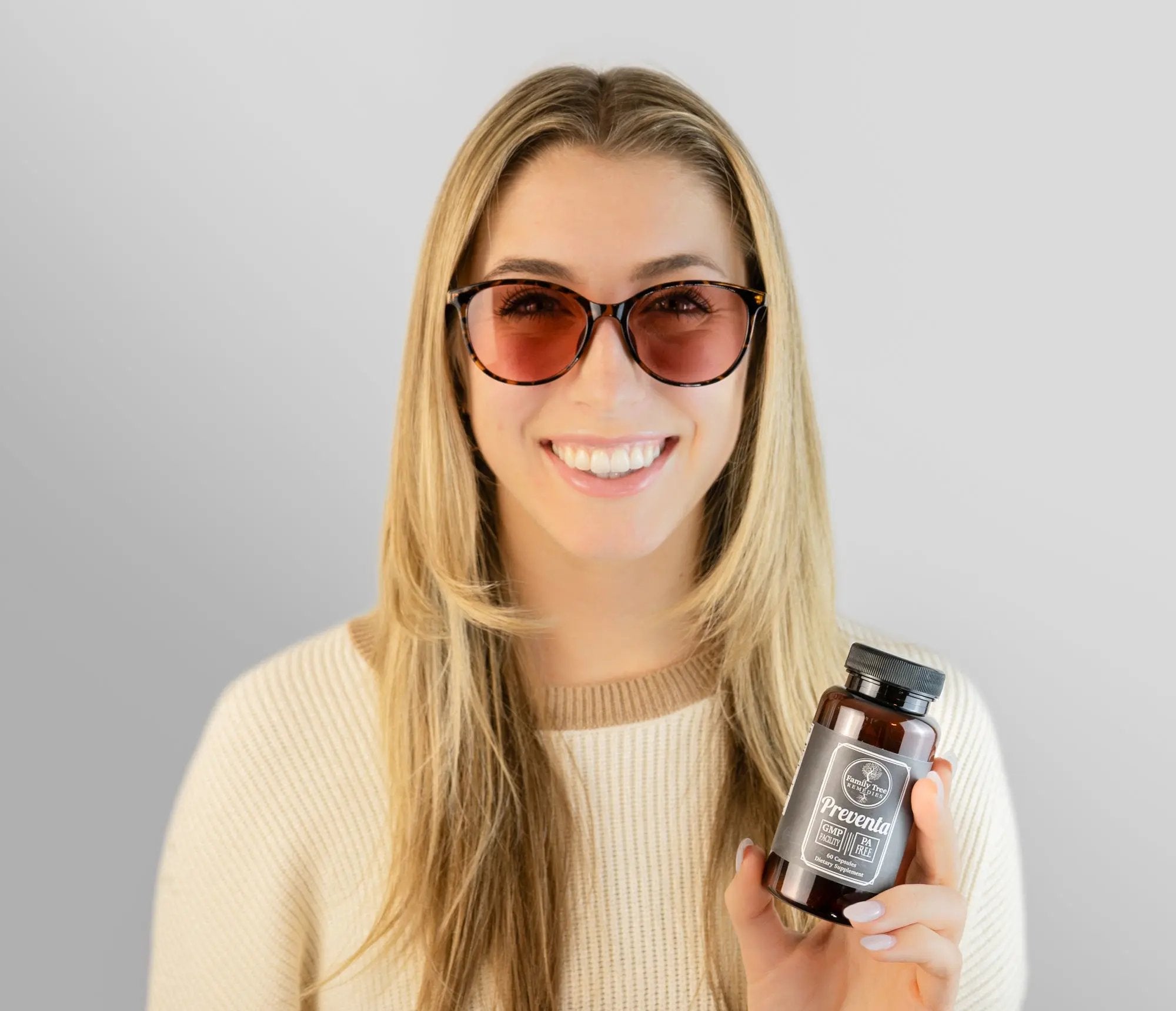 Smiling woman wearing Eclipse Aura FL-41 glasses, holding a bottle of Preventa